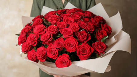 Woman holding bouquet of fresh red roses on light background, closeup